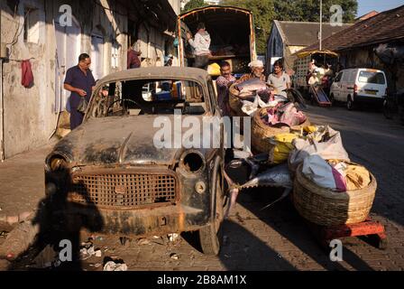 À côté d'une vieille voiture épatée, des vendeurs de poissons chargent du poisson dans un camion, au port de pêche de Sassoon Docks, à Colaba, Mumbai, Inde Banque D'Images