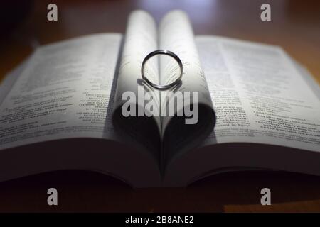 Anneaux de mariage sur une bible avec ombre formant une forme de coeur Banque D'Images