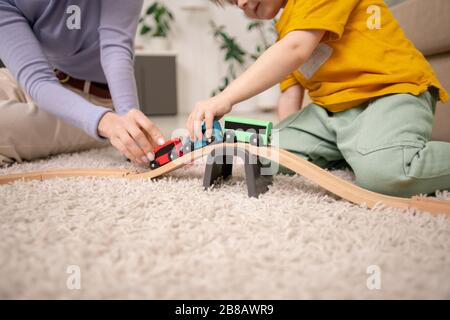 Gros plan de la mère et du fils assis sur la moquette et jouant avec le train jouet sur le chemin de fer jouet Banque D'Images