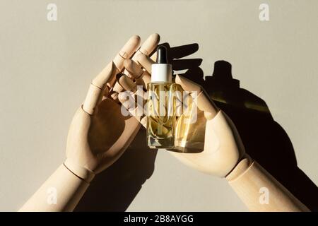 Les mains en bois contiennent une bouteille d'huile organique naturelle à base de sérum de collagène. Concept créatif de soins spa. Composition minimaliste avec ombre. Banque D'Images