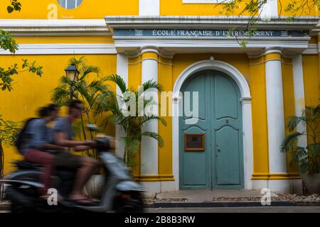 Pondichéry, Inde - 17 mars 2018 : couple inconnu sur un scooter qui passe devant un bâtiment scolaire jaune avec flou de mouvement Banque D'Images