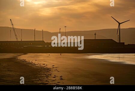 Swansea, Royaume-Uni, 21 mars 2020. Un marcheur de chien solitaire fait son chemin à travers la plage déserte en face des quais de Swansea à Swansea, au sud du Pays de Galles ce matin. Crédit: Phil Rees/Alay Live News Banque D'Images