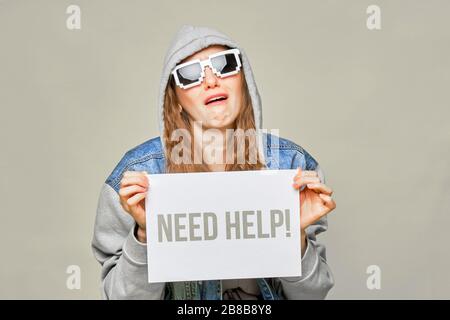 Fille caucasienne élégante en Jean et lunettes 8 bits sur fond jaune. Tenir un morceau de papier blanc dans ses mains avec l'inscription a besoin d'aide. C Banque D'Images