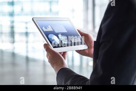 Homme lisant des statistiques financières, des graphiques commerciaux et des données commerciales. Homme d'affaires utilisant une tablette dans un immeuble de bureaux moderne. Banque D'Images