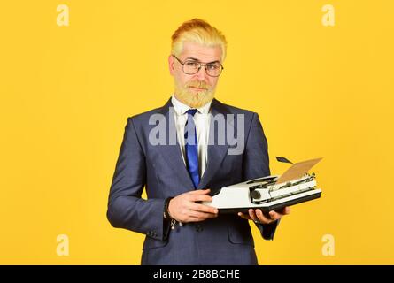 Magasin de marchandises d'occasion. Objets anciens du vendeur. Connaisseur des valeurs vintage. Machine à écrire vintage. Les hommes d'affaires utilisent la technologie rétro. Homme mûr teint les cheveux de barbe fond jaune. Les vieux habitudes de l'auteur de bâton. Banque D'Images
