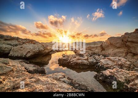 Beau coucher de soleil coloré près de la mer à Chypre avec des nuages et des rochers spectaculaires. Réflexions dans l'eau. Beauté monde nature extérieur voyage fond Banque D'Images