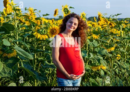Une belle photo d'une heureuse femme enceinte debout dans un champ avec beaucoup de tournesols sur une journée ensoleillée.famille enceinte photo de la nature Banque D'Images