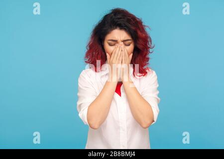 Portrait d'une femme bouleversée avec des cheveux rouges fantaisie dans une chemise se cachant le visage dans les mains et pleurant, essuyant les larmes, éprouvant la dépression, les émotions désespérées méchantes Banque D'Images