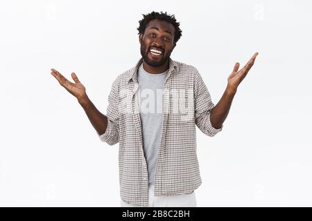 Un jeune homme afro-américain ordinaire et insouciant, se tenant debout avec sobriété et sans peine, se levant les mains sur les côtés haussant les épaules et les souriants, souriants et amusés Banque D'Images