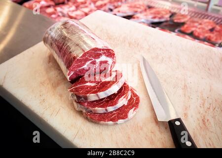 Viande de steak à l'œil de côtes crues en tranches et couteau sur le tableau de découpe dans un magasin de boucherie Banque D'Images