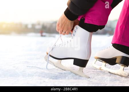 Une femme qui liait des patins à glace à lacets au bord d'un lac ou d'un étang. Laçage iceskates. Skater est sur le point de faire de l'exercice sur une piste ou une patinoire extérieure. Temps ensoleillé d'hiver. Banque D'Images