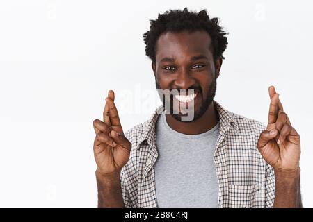 Portrait rapproché homme porteur d'espoir, optimiste et gai afro-américain ayant foi dans les rêves deviennent réalité, croisez les doigts pour bonne chance, priant Banque D'Images