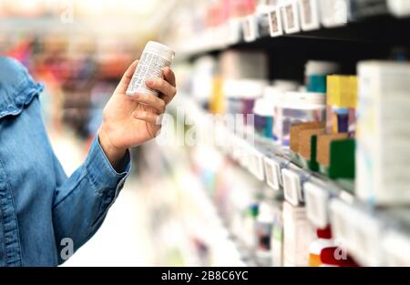 Client en pharmacie contenant la bouteille de médicaments. Femme lisant le texte de l'étiquette au sujet de l'information médicale ou des effets secondaires dans le magasin de drogue. Achats de patients. Banque D'Images