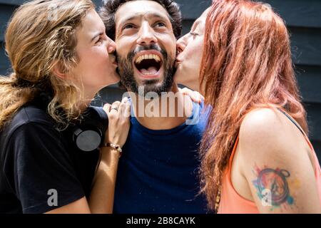 Deux jeunes femmes donnant un baiser sur chaque joue à un jeune homme d'origine ethnique différente avec une barbe et une moustache dans la rue Banque D'Images
