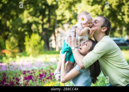 Les jeunes parents heureux marchent, jouent et embrassent leur petite fille dans le parc le jour clair de l'été. Concept de « Happy Family Time Together » Banque D'Images