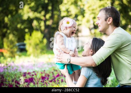 Les jeunes parents heureux marchent, jouent et embrassent leur petite fille dans le parc le jour clair de l'été. Concept de « Happy Family Time Together » Banque D'Images