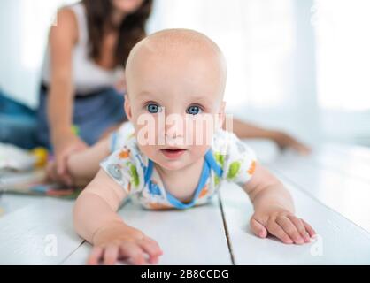 Un charmant bébé de six mois se cramille sur le sol en toile de fond avec ses parents joyeux et flou. Le concept de préparation de la première étape de la b Banque D'Images
