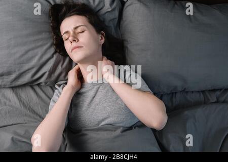 Top vue rapprochée bouleversée la jeune femme couché au lit le matin ressent des douleurs dans le cou après le sommeil de nuit, se réveillent en ayant des douleurs soudaines ou de la raideur Banque D'Images