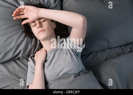 Vue de dessus sur la jeune femme malheureuse avec les yeux fermés allongé dans le lit, touchant la main du front ayant une migraine souffrant, se sentant mal Banque D'Images