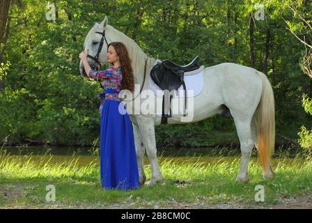 Jeune femme en mode robe de marche avec cheval de selle dans les bois de printemps Banque D'Images