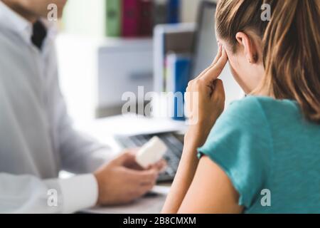Médecin donnant de l'aide médicale à un patient malade souffrant de mal de tête ou de migraine. Médecin ou pharmacien tenant une bouteille de pilules et de médicaments en rendez-vous. Banque D'Images