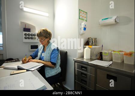 En service. Infirmière assise à la station d’une infirmière et écriture dans un document Banque D'Images