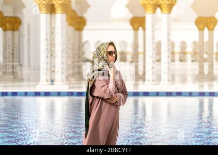 Femme dans la grande mosquée de Sheikh Zayed devant l'eau. Décor islamique. Touriste féminin dans le pays musulman. Tourisme, voyage et gens en vacances. Banque D'Images