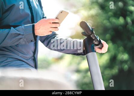 Homme d'affaires louant un scooter électrique avec smartphone dans le parc de la ville. Hipster man utilisant un service de location de téléphone mobile intelligent dans la rue urbaine. E véhicule. Banque D'Images