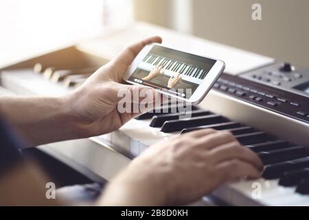 Cours de piano en ligne. Homme regardant un didacticiel vidéo avec un téléphone mobile et pratiquant la lecture. Personne apprenant à jouer un instrument. Banque D'Images