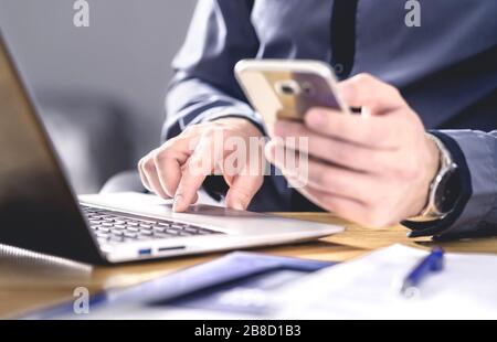 Multitâche et technologie mobile. Homme d'affaires professionnel occupé utilisant le téléphone et l'ordinateur portable. Entrepreneur travaillant dur avec smartphone et ordinateur. Banque D'Images