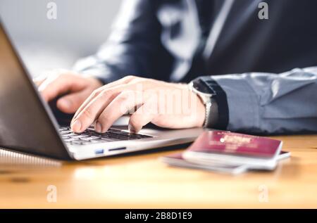 Homme avec passeport et ordinateur portable. Document de voyage et identification. Immigrants écrivant une demande électronique de citoyenneté. Demandez un visa numérique. Banque D'Images