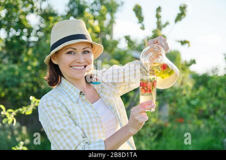 Rafraîchissements d'été de printemps, femme dans la nature tenant pot de menthe de fraise et citron, boissons rafraîchissantes froides, boissons saines de vitamine maison Banque D'Images