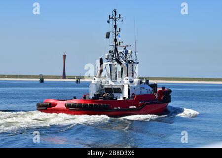 Bateau à remorqueur moderne rouge vif dans le port de Rotterdam en toile de fond d'une tour radar construite en acier moderne Banque D'Images