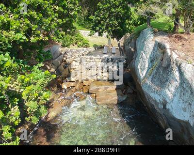 Vue aérienne d'un petit jardin tranquille avec des chaises en bois entre les rochers et à côté de l'eau claire de cristal de l'océan dans le pays tropical. Brésil Banque D'Images