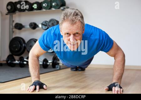 Homme souriant mûr faisant des poules dans une salle de gym - se concentrer sur le visage Banque D'Images