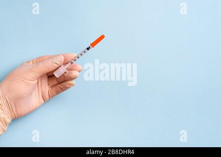 La main de la femme dans les gants médicaux maintient la seringue sur un fond bleu clair avec ombre douce, espace de copie. Concept de médecine et de santé. Banque D'Images