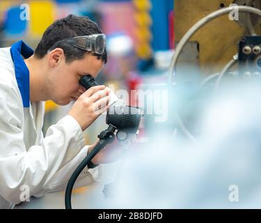 l'ingénieur vérifie le réglage correct du moule métallique pour les pièces moulées en usine à l'aide d'un microscope Banque D'Images