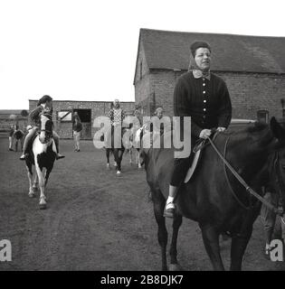 1963, historique, femme et enfants sur les chevaux dans une cour d'une école d'équitation, Angleterre, Royaume-Uni. Banque D'Images