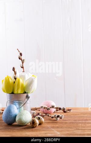 Félicitation composition festive de fleurs de tulipes fraîchement cueillies dans un seau et œufs peints à la main sur une table en bois contre l Banque D'Images