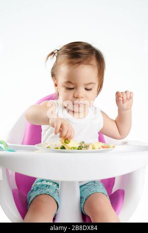 Bbay fille choisir la nourriture de l'assiette isolée sur fond de studio blanc Banque D'Images