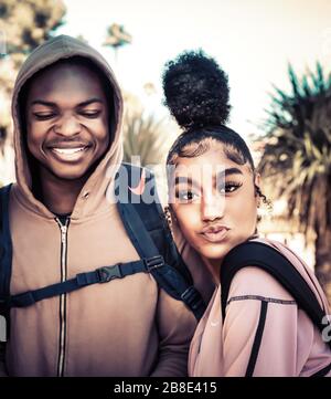 Un homme d'Afrique américain d'âge universitaire à hoodie le long d'un beau coed féminin de couleur avec cool up-do branché sur le campus en profitant de la vie d'étudiant Banque D'Images