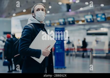 Homme voyageur porte un masque médical jetable de protection à l'aéroport, les retours de l'étranger où le coronavirus se propage, porte sac à dos, prend soin de la hea Banque D'Images