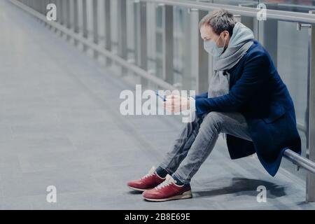 Les touristes fatigués se brisent, utilisent le téléphone mobile, vêtu d'une veste, d'un Jean et de baskets, portent un masque de protection contre le coronavirus, se soucie de la santé Banque D'Images