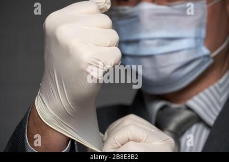 un homme avec un masque sur son visage pour la protection individuelle antivirus met sur des gants médicaux stériles - concept de santé et de médecine, des conseils de prévention Banque D'Images