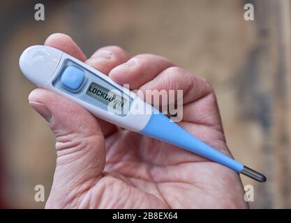 La main masculine tient un thermomètre clinique avec du texte de verrouillage à l'écran pendant la pandémie mondiale de covid-19 ou de corona Banque D'Images