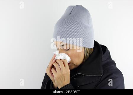 Femme malade portant un bonnet et utilisant un tissu pour éternuer et souffler son nez. Banque D'Images