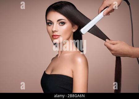 Coiffure le redressage de longs cheveux noirs avec des fers de cheveux. Belle femme avec de longs cheveux raides. Coiffure lisse Banque D'Images