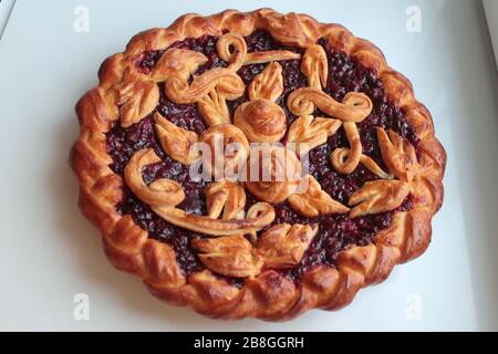 Délicieuse tarte ronde dorée aux cerises rouges et aux mûres de lingonberry avec motif de pâte sur fond blanc. Banque D'Images