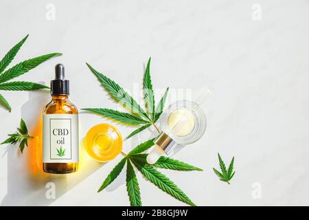 Bouteille brune de verre avec de l'huile de cannabis CBD avec étiquette et des feuilles de marijuana sur un fond de marbre. Espace de copie Banque D'Images
