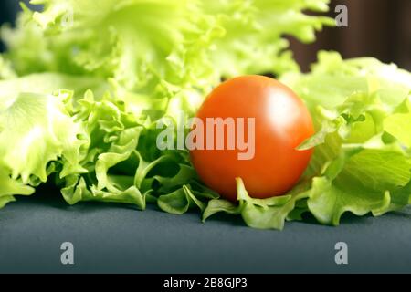 Les tomates cerises et la laitue se trouvent sur une surface sombre. Tomates cerises mûres. Les tomates sont sur la table. Tomate coupée en tranches. Tomates cerises coupées en deux. Banque D'Images